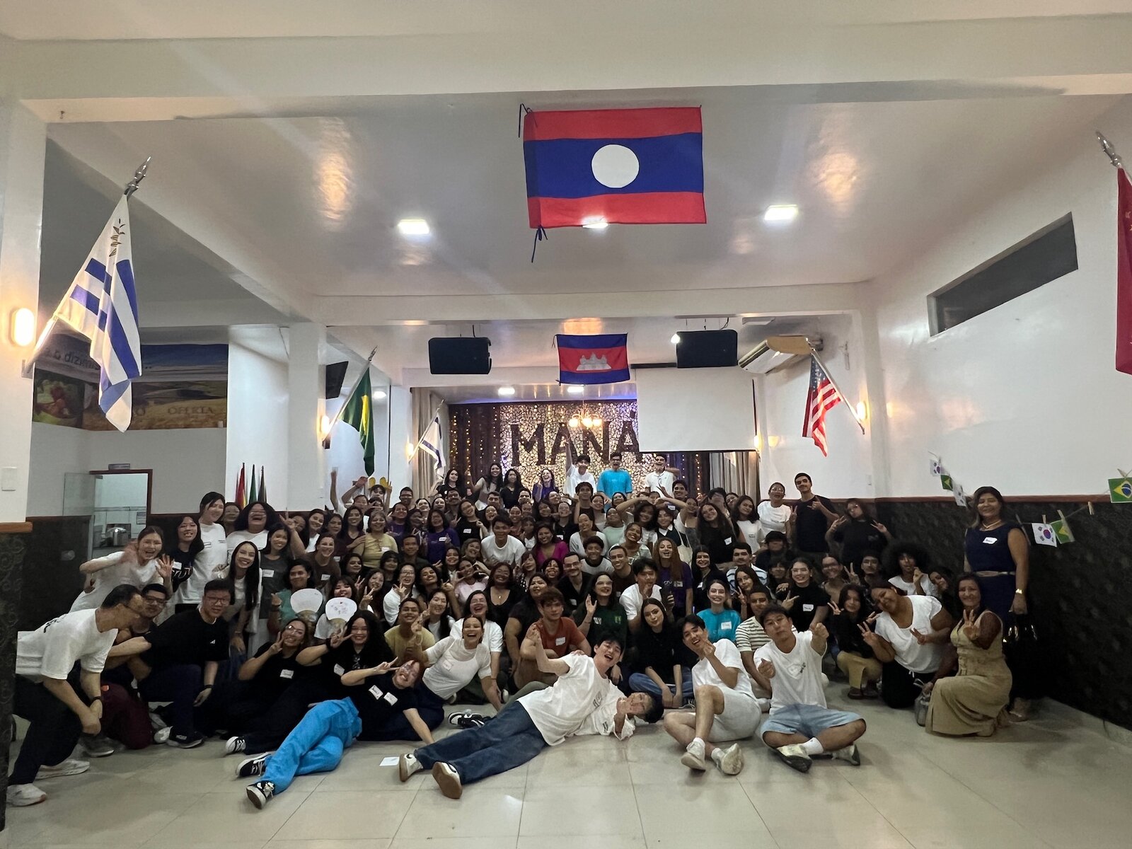 A large group gathered under international flags at a Mana event in Brazil